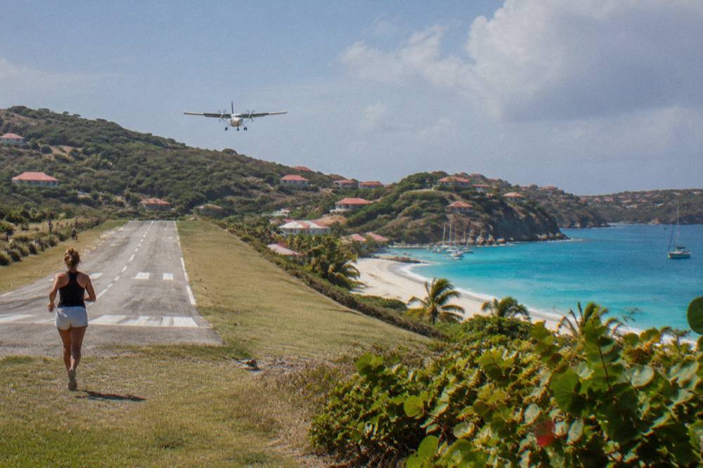 A small turboprop aircraft on a short runway between a beach and green hills