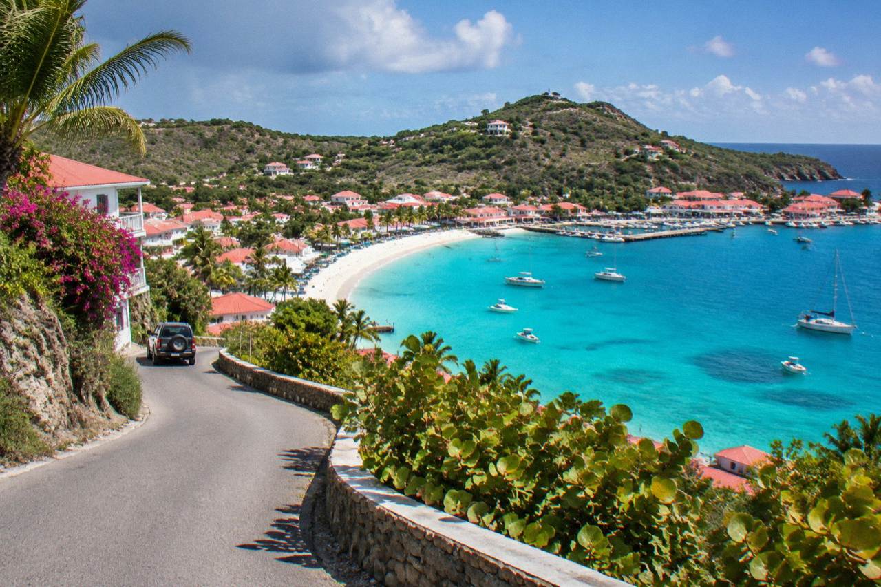 A narrow winding road climbing a green hillside above the turquoise sea on a Caribbean island