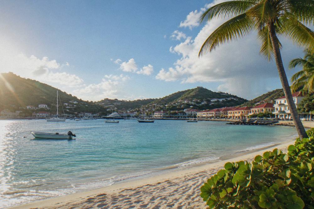 White sand beach with calm turquoise water and a few palm trees on a small Caribbean island