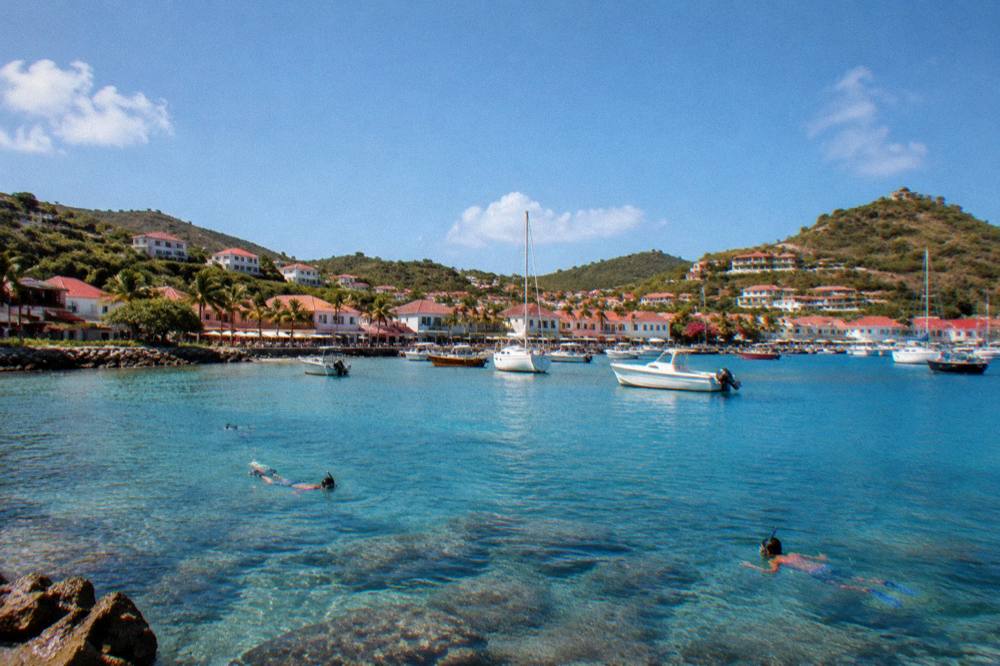 Snorkellers swimming over clear shallow water above rocks and coral