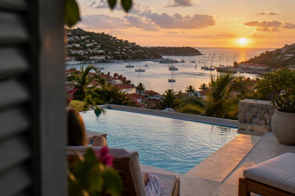 An evening view of a lit swimming pool and terrace above a darkening Caribbean sea