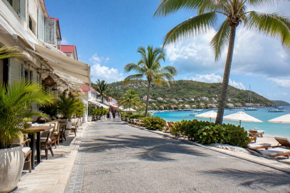 Lounge chairs and umbrellas on white sand beside a calm turquoise bay