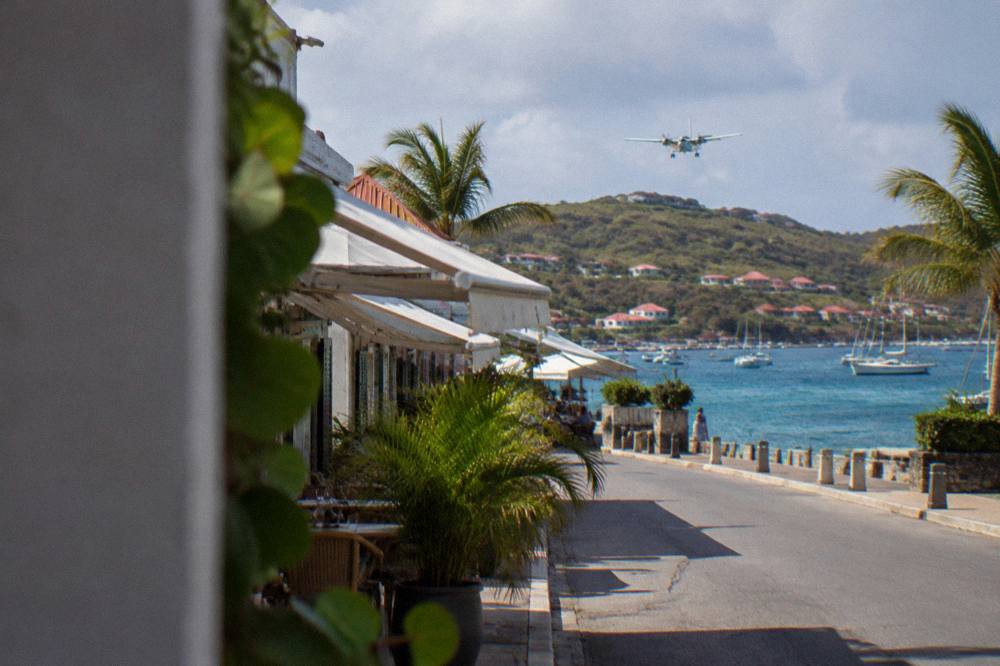 A small turboprop aircraft descending over a hill toward a Caribbean seaside runway
