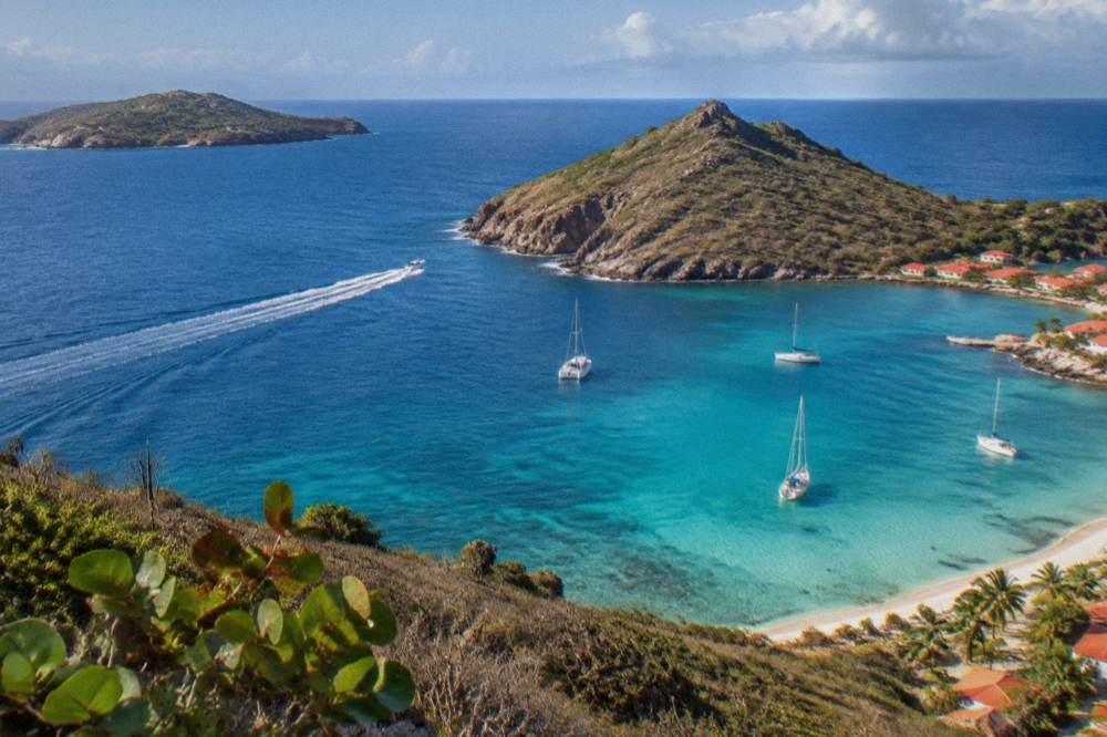 A speedboat crossing open blue water between two islands