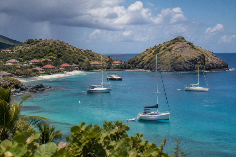 Yachts at anchor in a harbor with wooded hills behind