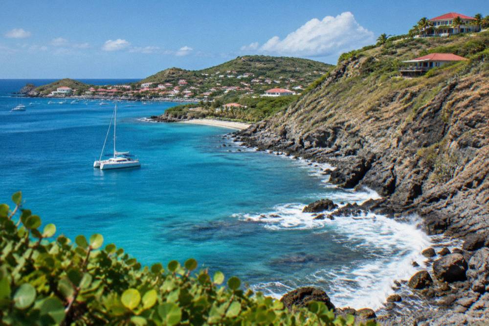 A small sailing catamaran anchored in a clear bay below green hills