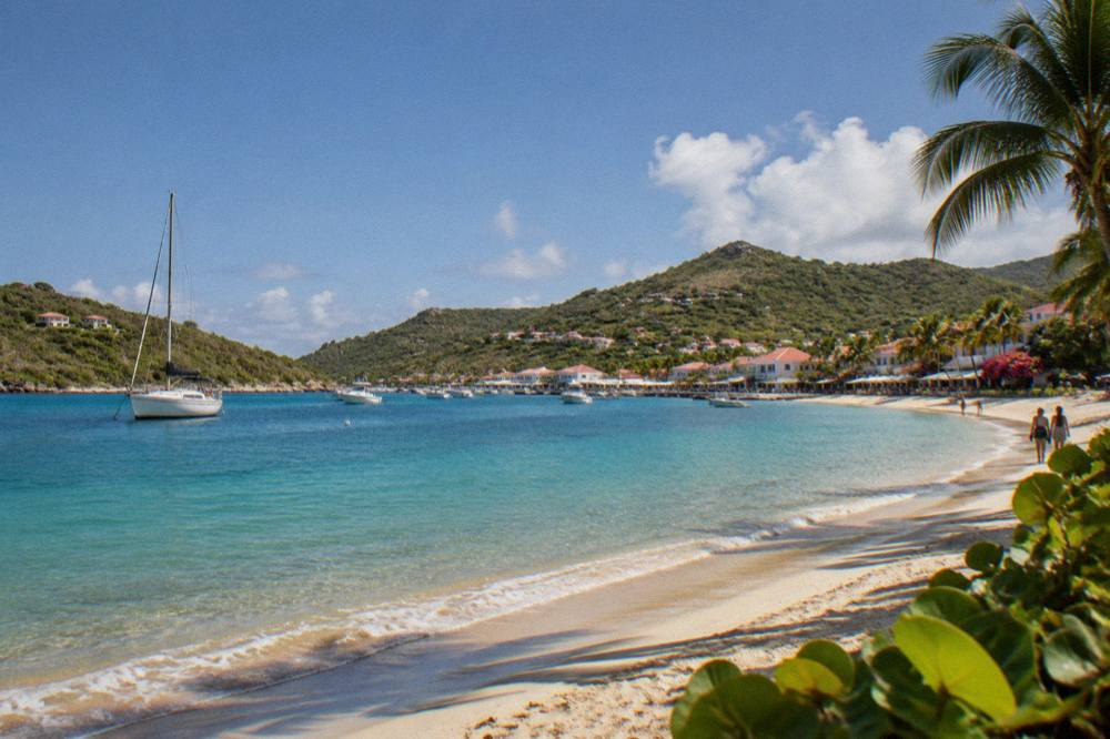 A sailboat anchored in a clear bay with green hills rising behind it