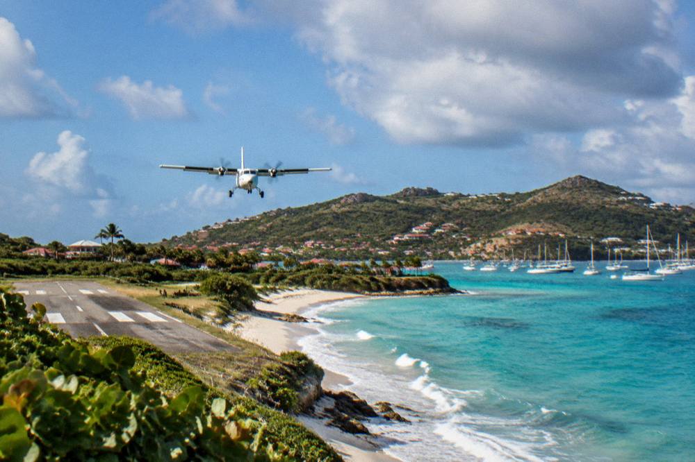 A small turboprop aircraft on a short runway beside a beach with hills behind