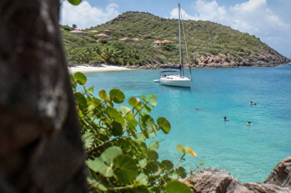 A sailboat anchored in a quiet bay with snorkelers in the water nearby