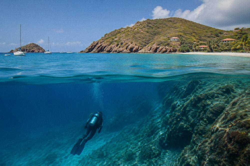 A diver descending along a rocky underwater slope with clear blue water above