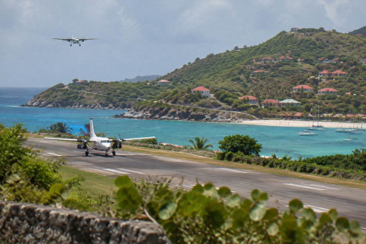 A small turboprop aircraft on the short runway at Gustaf III Airport in St Barts with green hills behind it