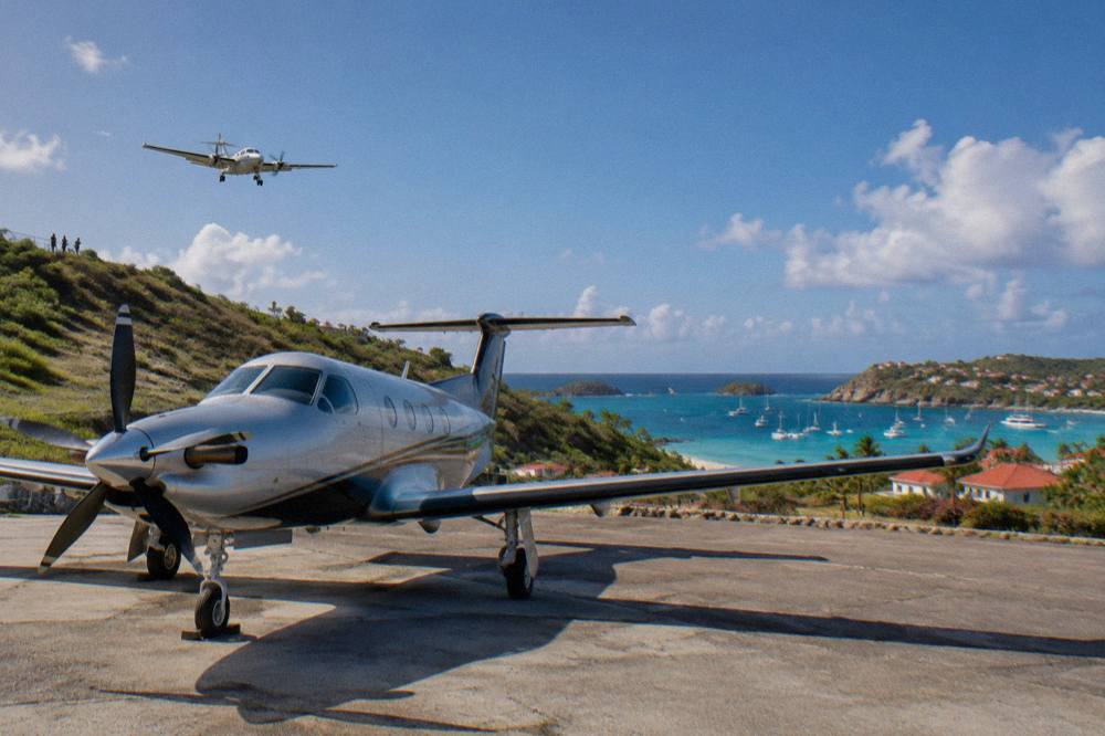A Pilatus PC-12 single-engine turboprop parked on an apron at a Caribbean airport