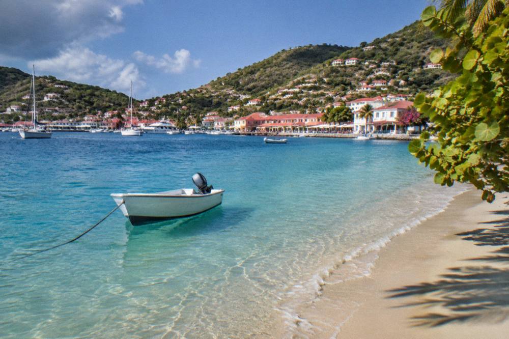 A small boat moored in clear shallow water beside a sandy beach in St Barts