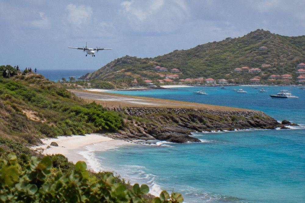 A small turboprop aircraft on the short runway at Gustaf III Airport in St Barts with green hills behind