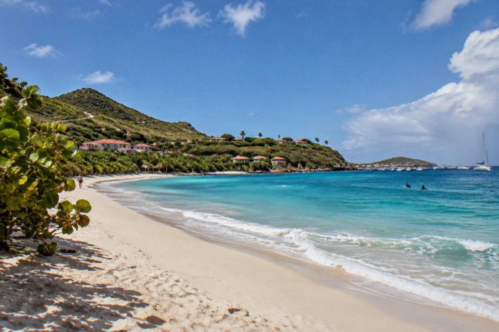 A narrow winding road with green hills descending toward a bay in St Barts