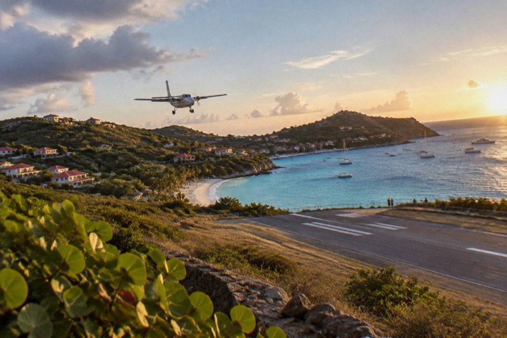 A small turboprop aircraft on a short runway beside a Caribbean beach