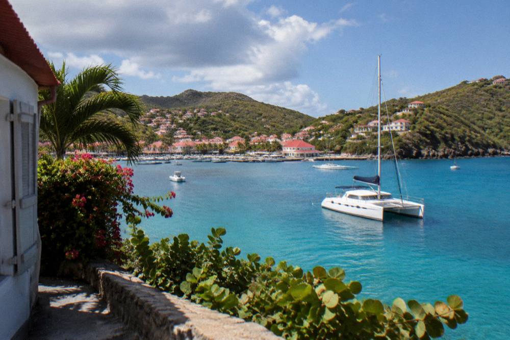 A sailing catamaran anchored in clear water beside a green headland