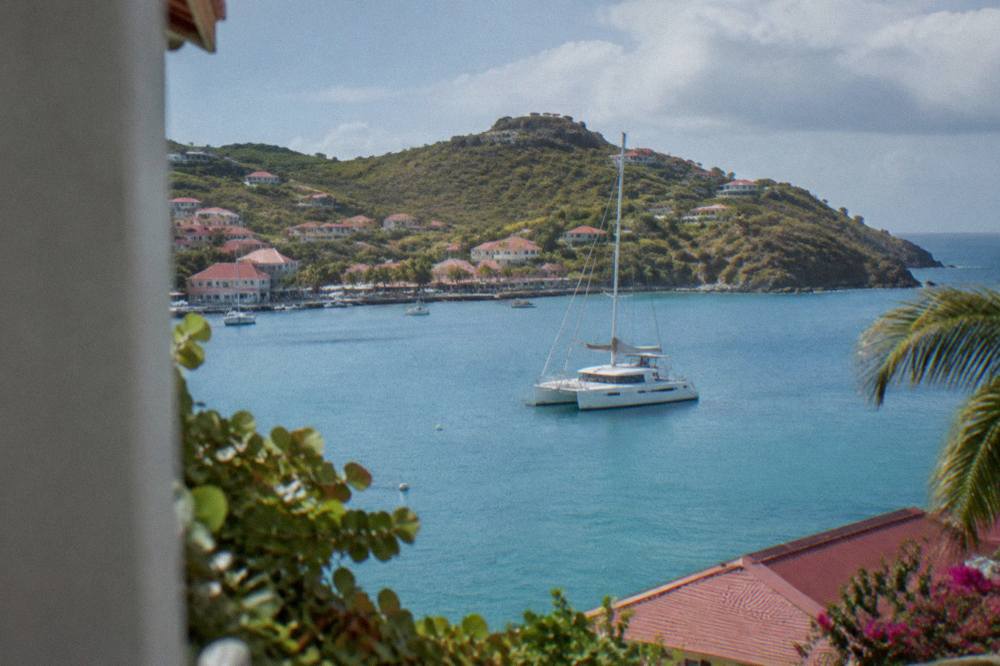 A sailing catamaran on calm blue water near a green island headland