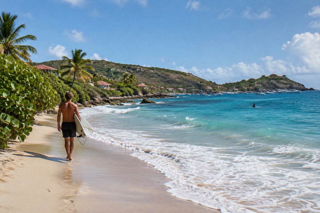 Surfer walking along a Caribbean beach with a board under one arm