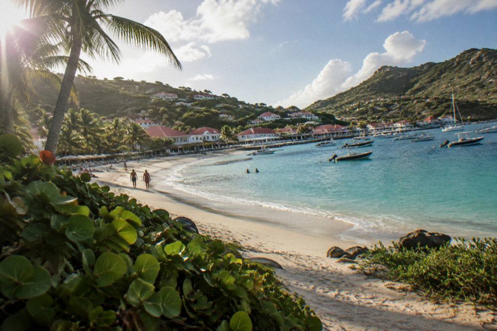 A sandy beach backed by green hills reached by a narrow path ending at the shoreline