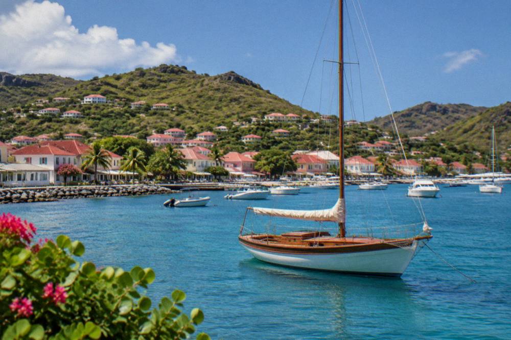 Wooden sailboat anchored in a quiet bay in St Barts with green hills behind
