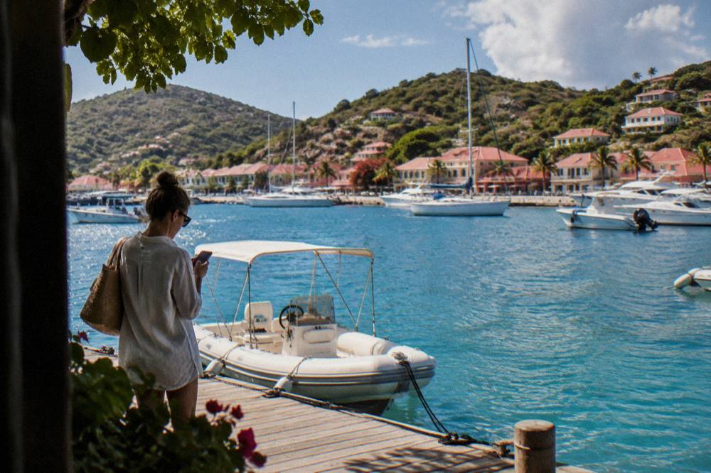 Traveler checking a phone beside a small boat docked at a wooden pontoon in the Caribbean