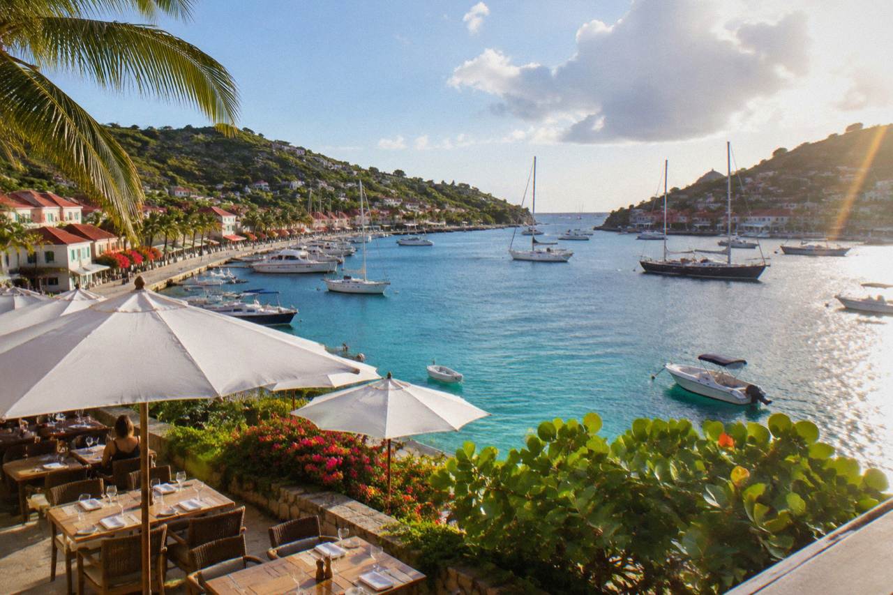 A harborfront terrace in Gustavia with cafe tables set for lunch and boats moored in the bay