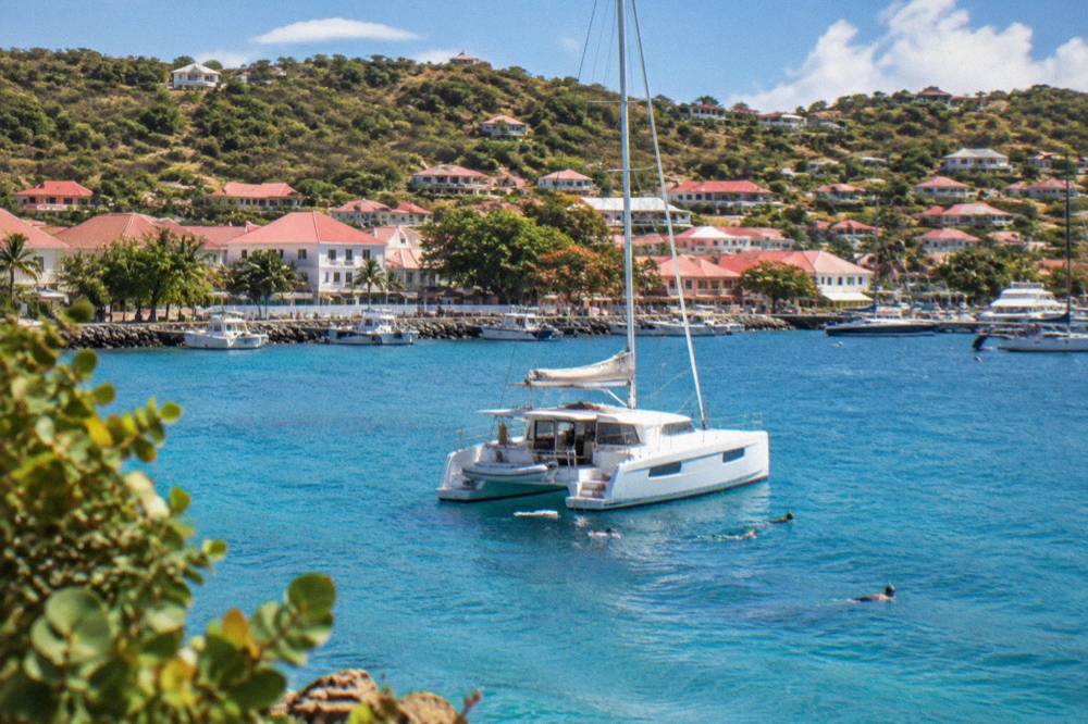 A sailing catamaran at anchor in a quiet bay with snorkelers in the water near the stern