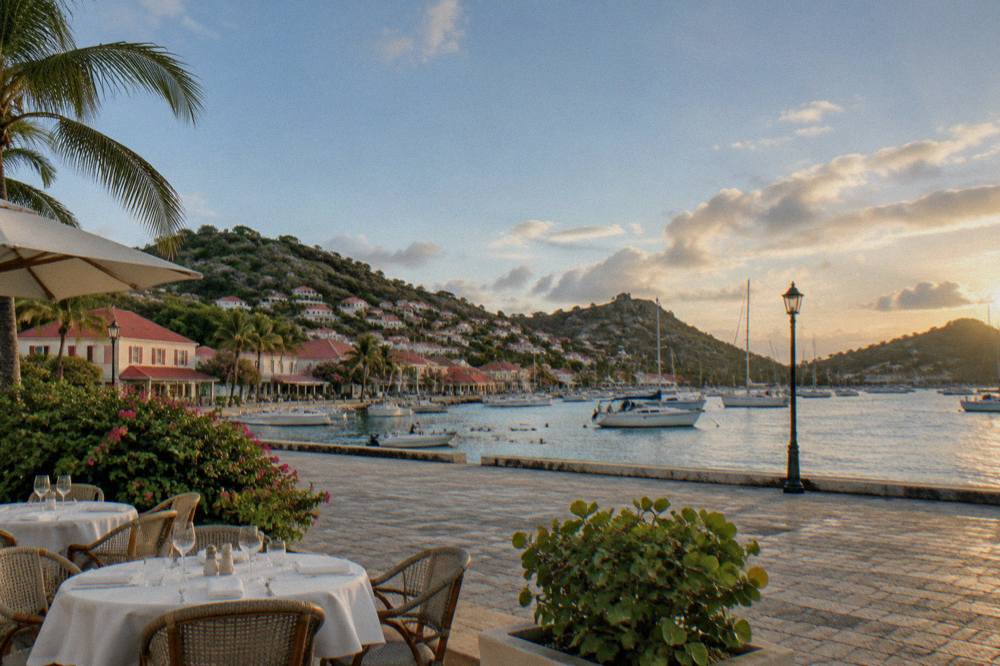 A quiet restaurant terrace with white tablecloths and an empty harbor square under a warm evening sky