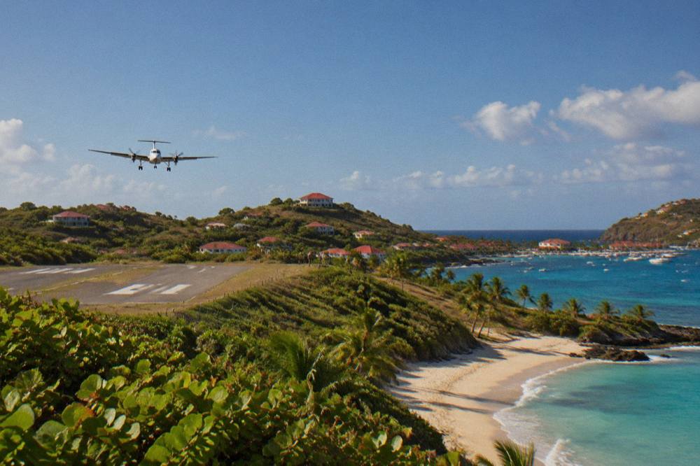 A small turboprop aircraft on a short runway beside a beach and green hill