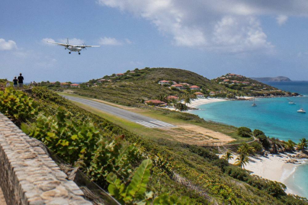 A small turboprop aircraft on a short runway beside a beach between green hills