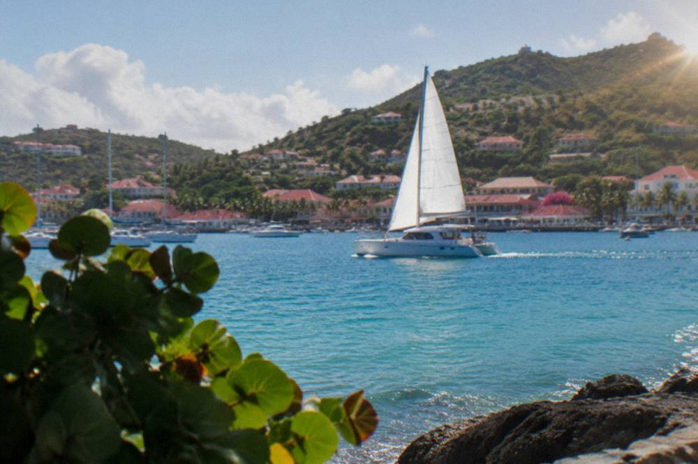 A catamaran with a raised white sail cutting across blue Caribbean water