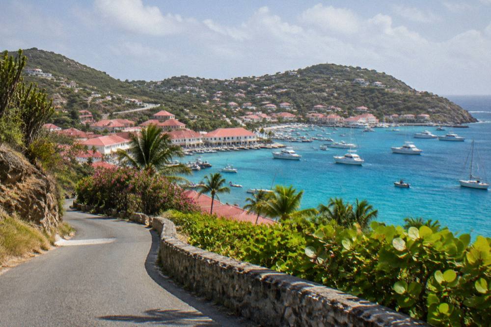 A hillside road curving down toward a bay with turquoise water in St Barts