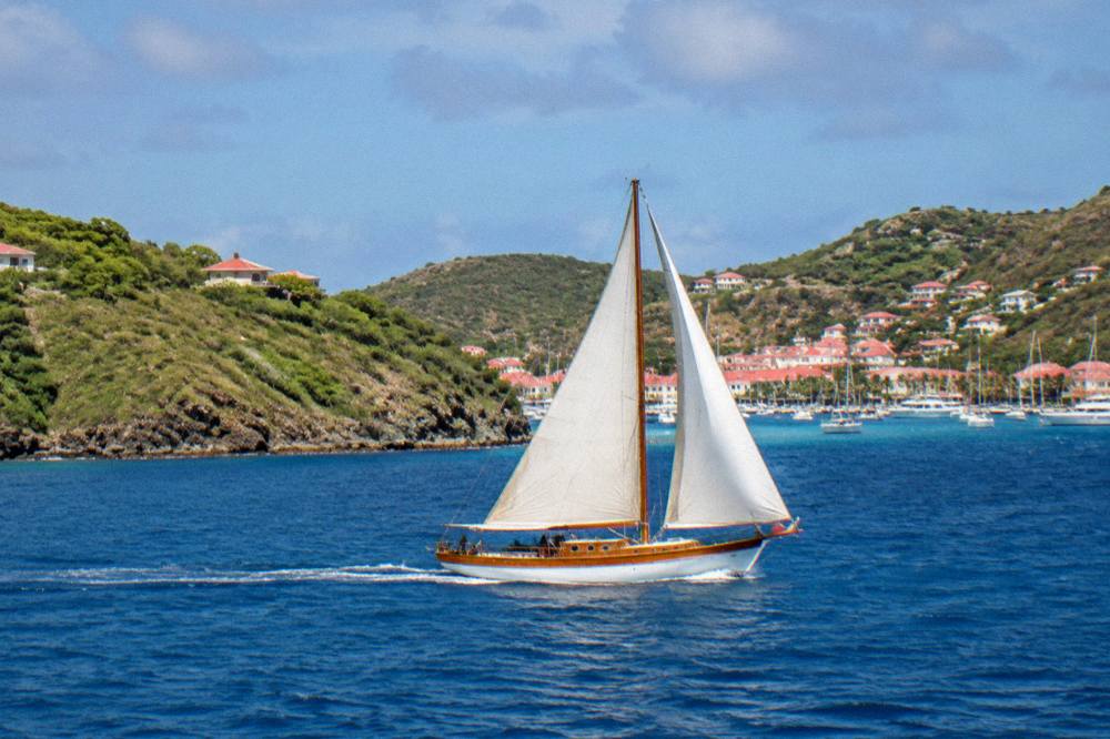 A wooden sailing boat crossing open blue water between two green islands