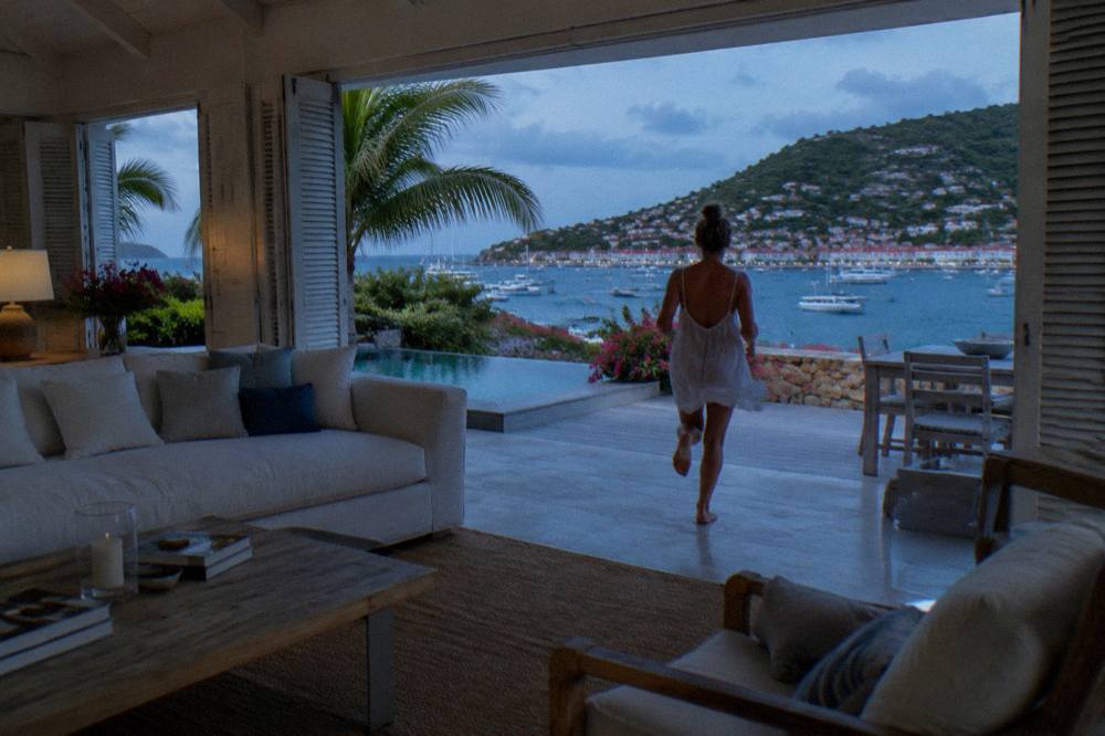 An open-plan villa living room with shutters open to a sea view