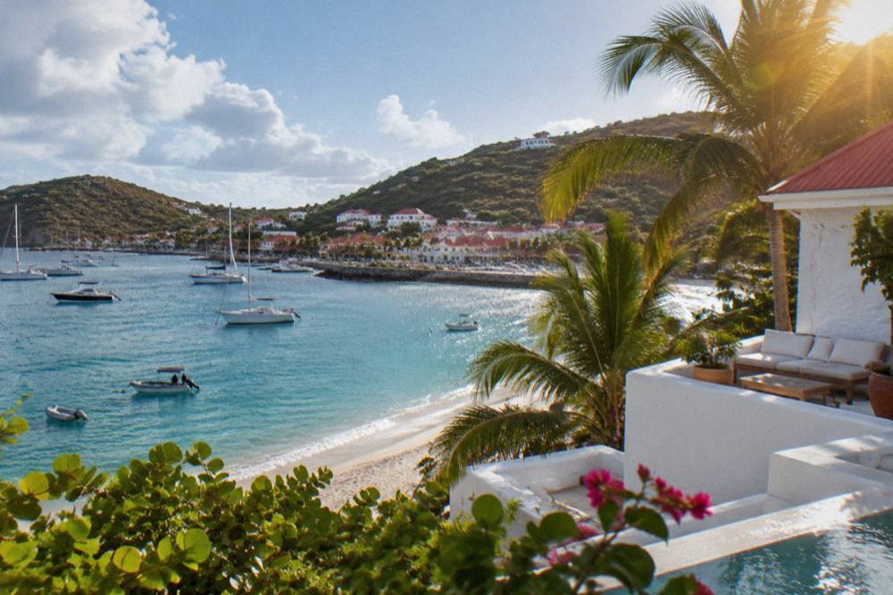 A whitewashed villa terrace with palms above a sandy bay in St Barts