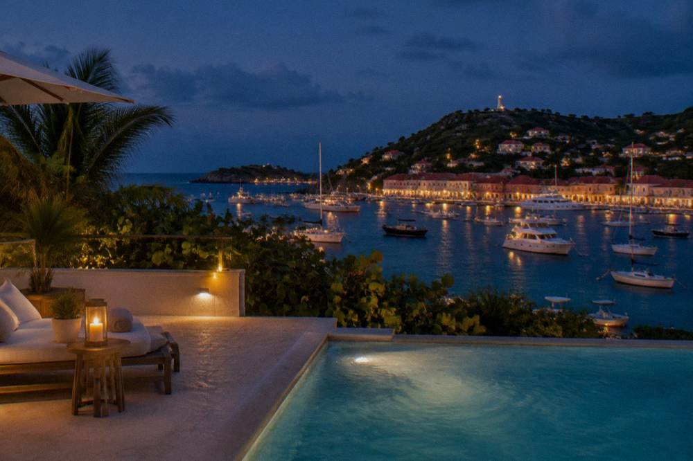 A villa pool terrace at dusk with the lights of Gustavia harbour below