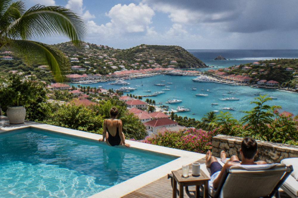 A family relaxing by a villa pool with the sea in the distance