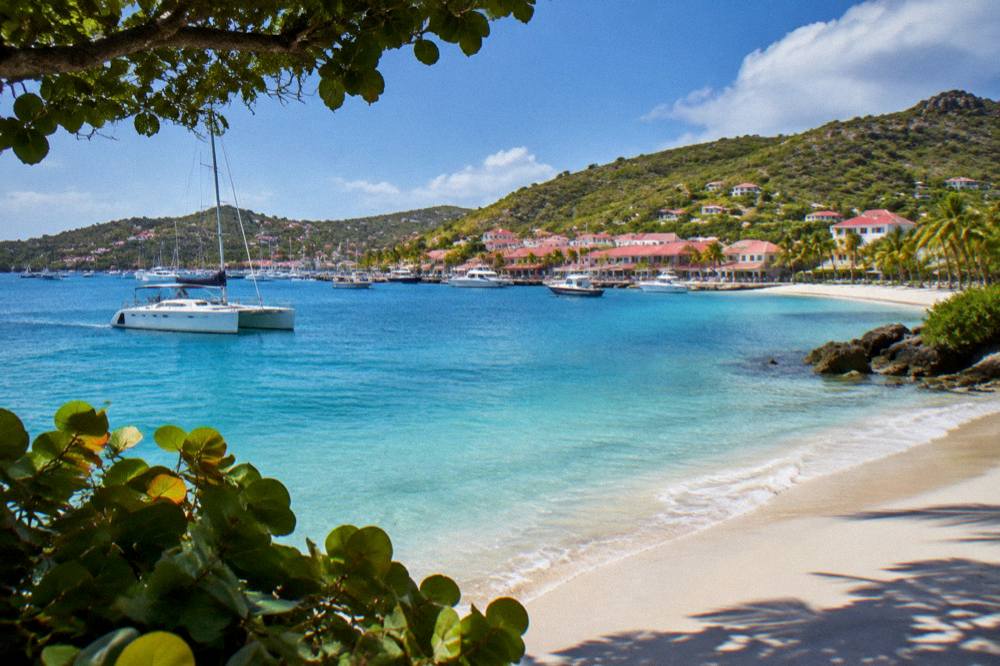 A catamaran anchored in a clear bay with a white sand beach in St Barts