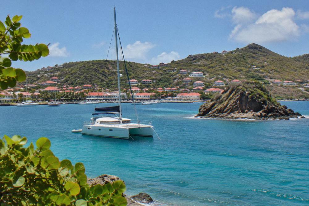 A sailing catamaran anchored in clear water near a rocky islet off St Barts