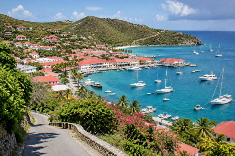 A narrow winding road with green hills descending toward a bay in St Barts
