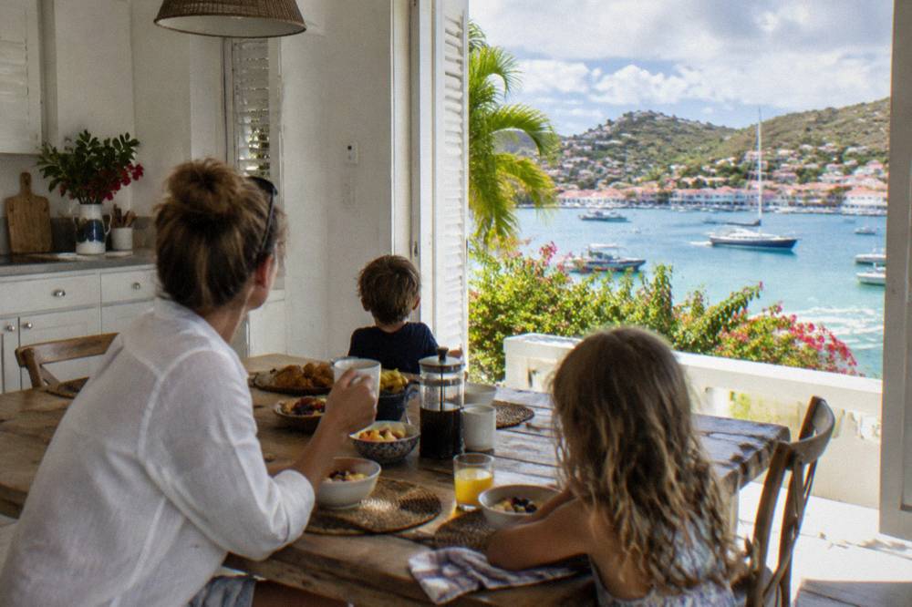 A villa kitchen with white cabinets and a wooden table set for a family breakfast