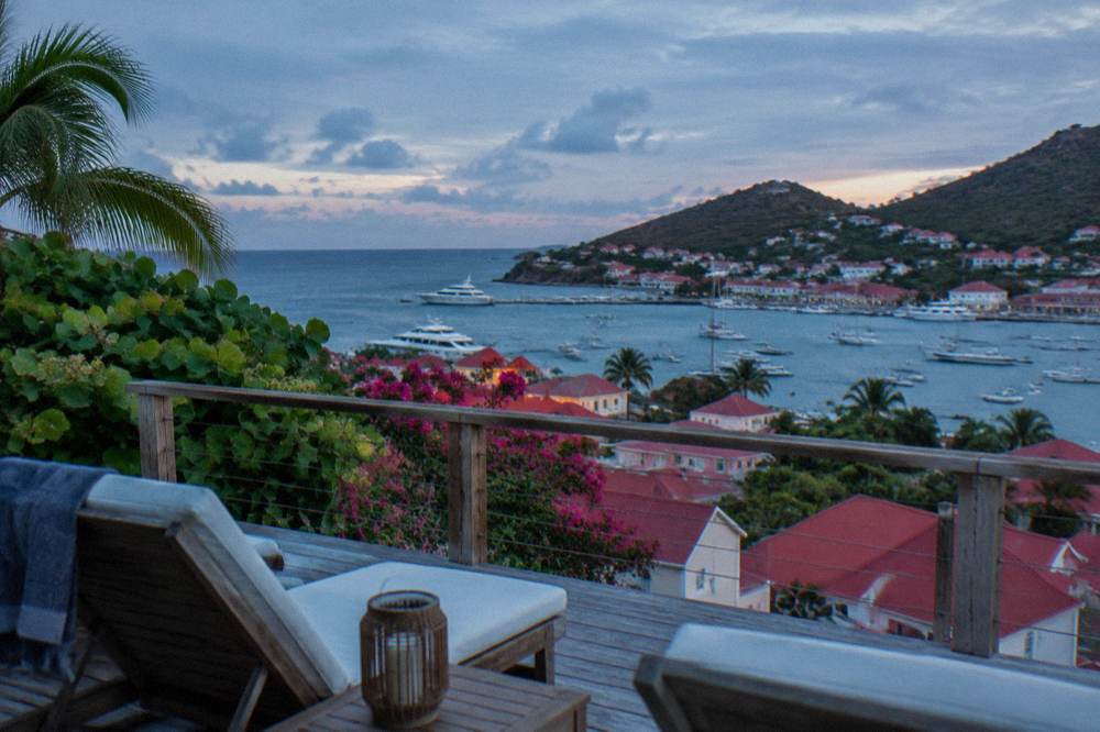 A wooden terrace with sun loungers and a view over red rooftops to the sea