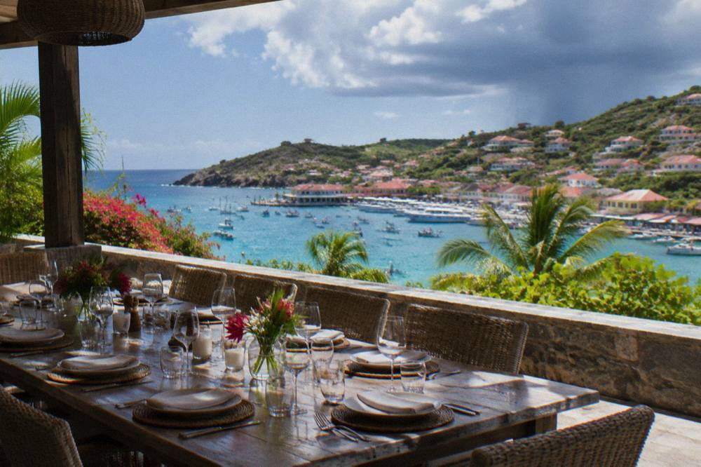 An outdoor dining table set for many guests on a shaded villa terrace above the sea