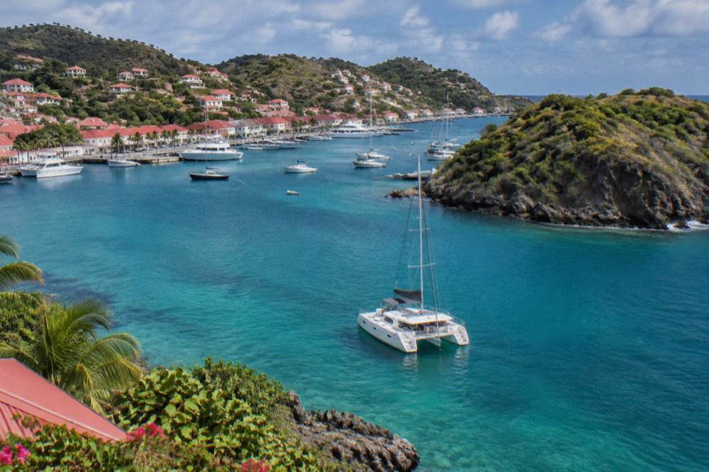 A catamaran anchored in clear water near a rocky green island