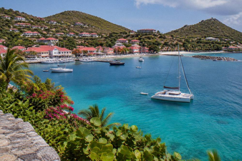 A sailing catamaran anchored in a clear bay with hills behind