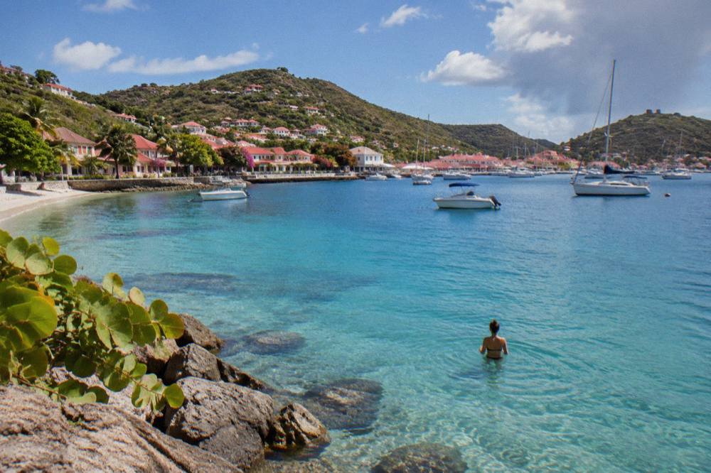 A swimmer standing waist deep in clear blue water near a St Barts shoreline
