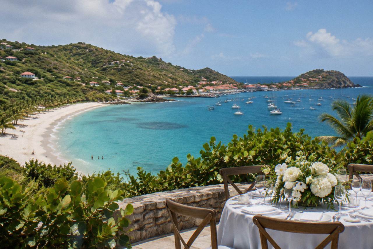 A wedding table set on a terrace above a Caribbean harbor with white flowers and an ocean horizon