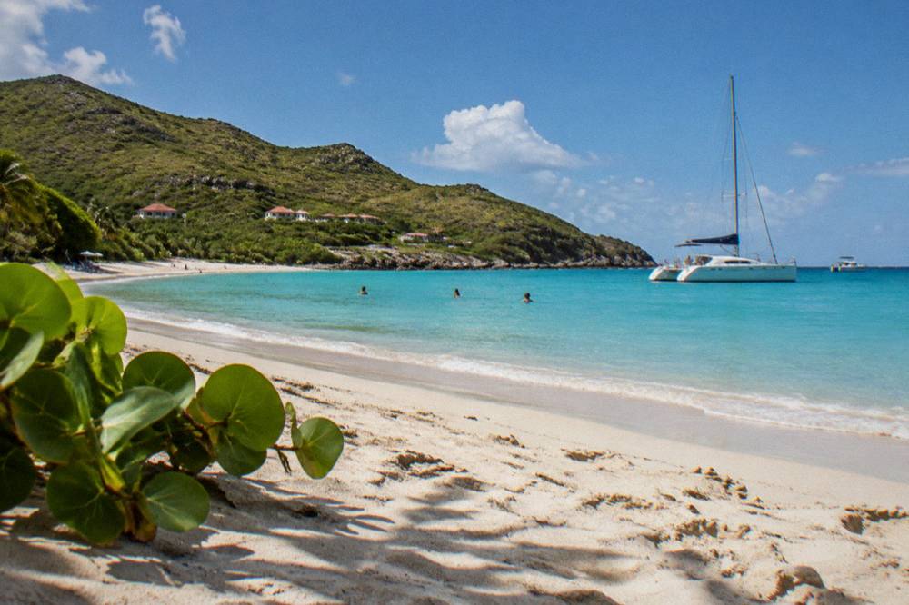 A sailing catamaran anchored in a calm bay with people swimming near the shore
