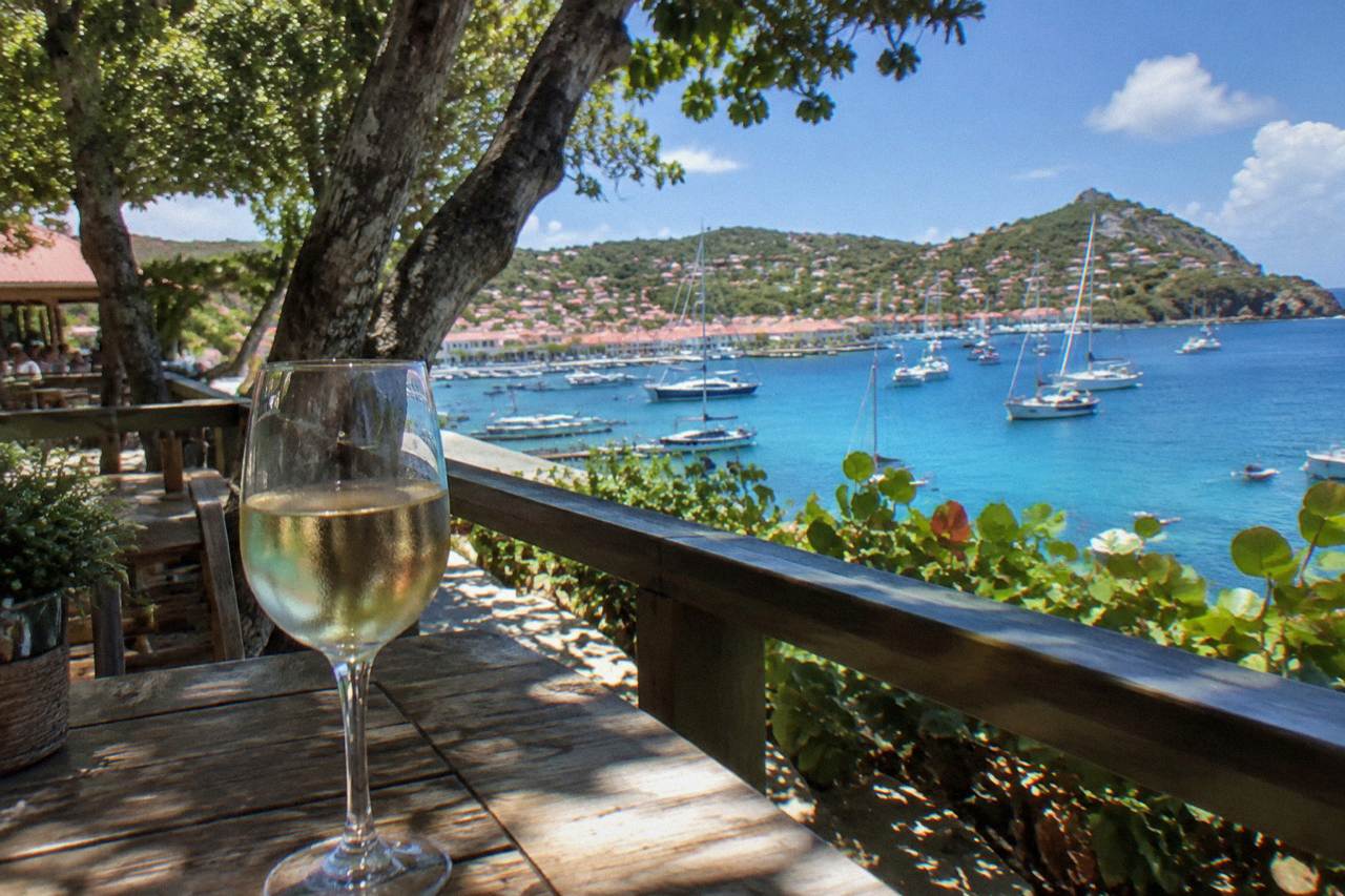A glass of white wine on a terrace above a Caribbean harbour with sailboats at anchor